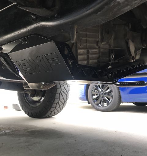 1995 Ford Bronco - The underside of a black aftermarket skid plate with the "BYF" logo is mounted to the frame of a vehicle. A portion of the vehicle's drivet…