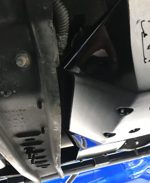 1995 Ford Bronco - A close-up, low-angle view of the underside of a vehicle frame, showing a black skid plate attached with bolts and screws. Visible text on…