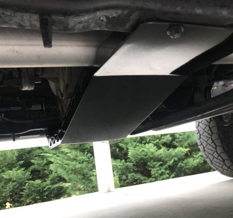 1995 Ford Bronco - The underside of a vehicle shows a black metal skid plate installed over the drivetrain components. The skid plate is bolted to the frame a…