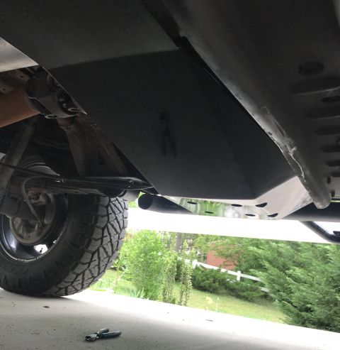 1995 Ford Bronco - Underside view of a black skid plate installed on a vehicle, with a tire and suspension components visible. The skid plate has several circ…