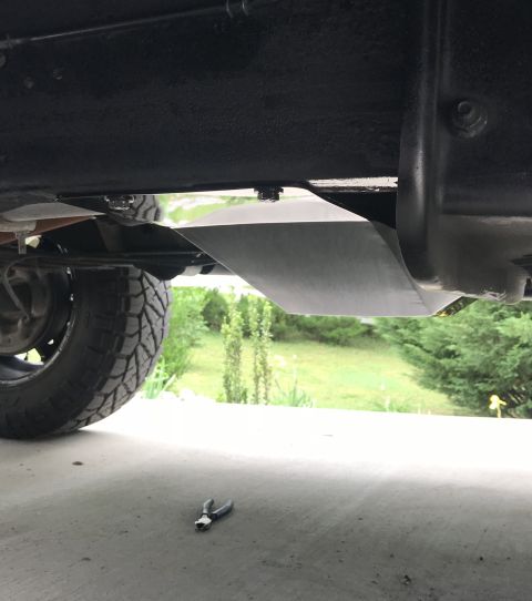 1995 Ford Bronco - Underside view of a vehicle showing a metal skid plate installed beneath the frame, with a tire visible on the left. A pair of pliers rests…