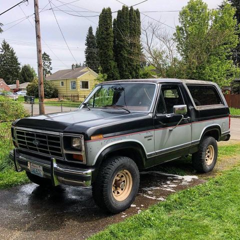 1986 Ford Bronco - This two-tone Ford Bronco is parked outside a residential home on a cloudy day.