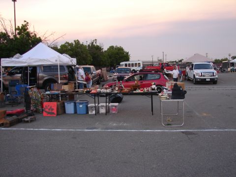 1973 Ford Ranchero - A red hatchback with a roof rack is parked at a flea market, surrounded by vendor tables and other vehicles.