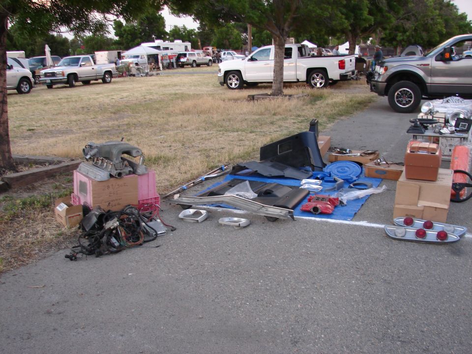 Car parts including an engine intake manifold, wiring harness, interior trim, and taillights laid out on a blue tarp