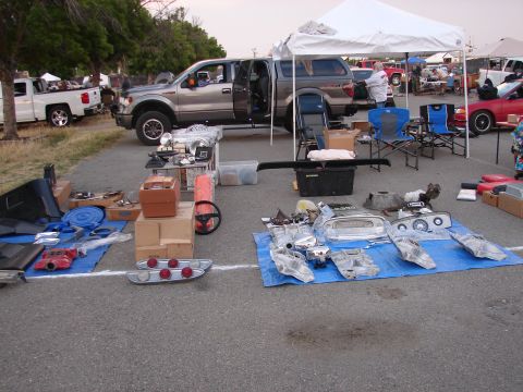 1973 Ford Ranchero - Various car parts are displayed on blue tarps at an outdoor market, with several trucks parked nearby.