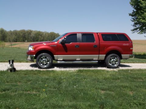2008 Ford F-150 - A red pickup truck with a cap is parked on a gravel driveway, with a dog sitting in the grass nearby.