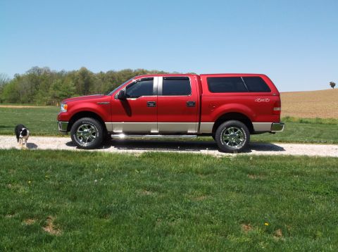 2008 Ford F-150 - A red pickup truck with a cap is parked on a gravel road next to a grassy field.