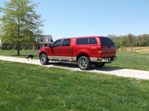 2008 Ford F-150 - Red Ford F-150 pickup truck with a camper shell parked on a gravel driveway near a house.