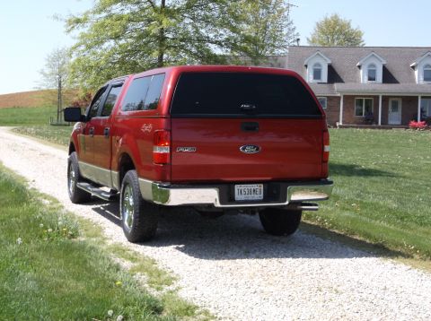 2008 Ford F-150 - Red Ford F-150 pickup truck with a camper shell seen from the rear on a gravel driveway.