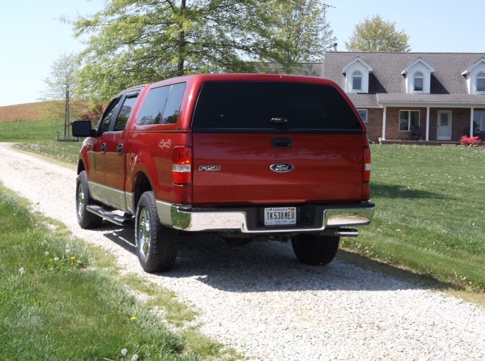 Rear view of a red Ford F-150 pickup truck with a camper shell, parked on a gravel driveway