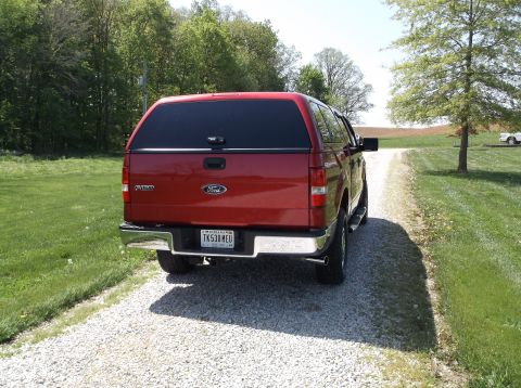 2008 Ford F-150 - Rear view of a red 2008 Ford F-150 pickup truck equipped with a cap, parked on a gravel driveway.