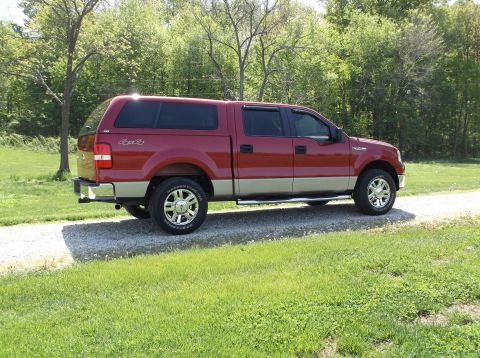 2008 Ford F-150 - This red 2008 Ford F-150 pickup truck is shown from the side, equipped with a camper shell and two-tone paint.