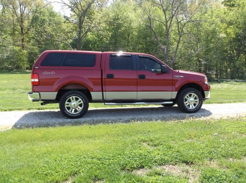2008 Ford F-150 - Red and tan Ford F-150 pickup truck with a camper shell parked on a gravel driveway.