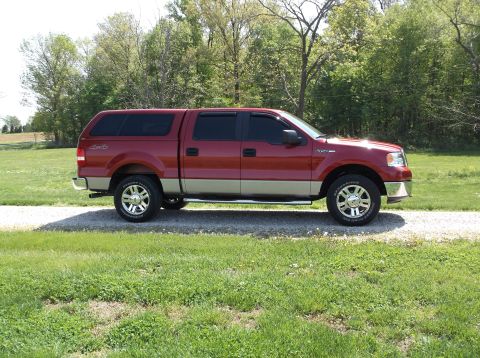 2008 Ford F-150 - This red Ford F-150 truck, equipped with a camper shell, is parked on a gravel driveway.