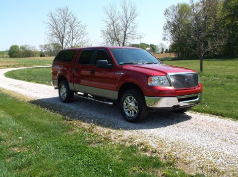 2008 Ford F-150 - Red Ford F-150 pickup truck with a cap on a gravel driveway.