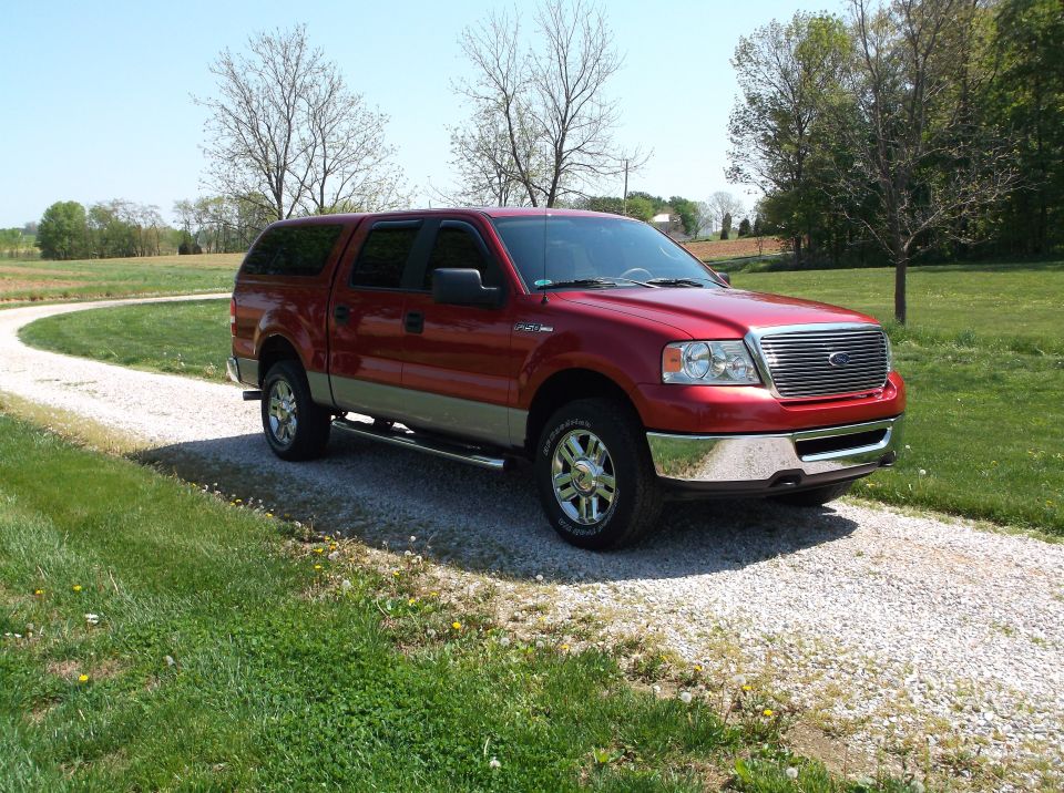 Red Ford F-150 pickup truck with a cap, parked on a gravel driveway