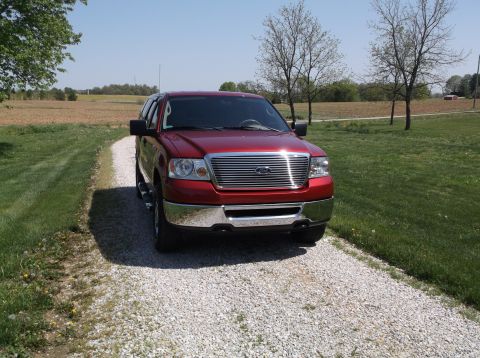 2008 Ford F-150 - Red Ford F-150 pickup truck on a gravel driveway with fields in the background.