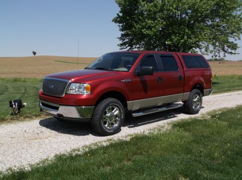 2008 Ford F-150 - A red 2008 Ford F-150 pickup truck with a camper shell is parked on a gravel driveway next to a grassy field.