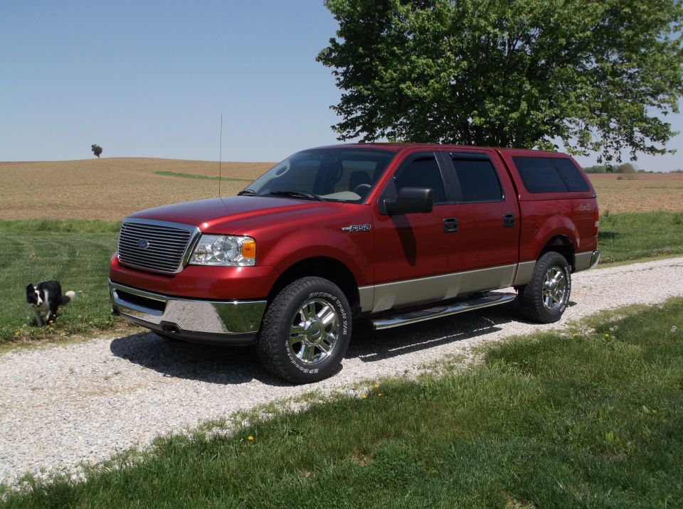 Red 2008 Ford F-150 with camper shell parked on a gravel driveway