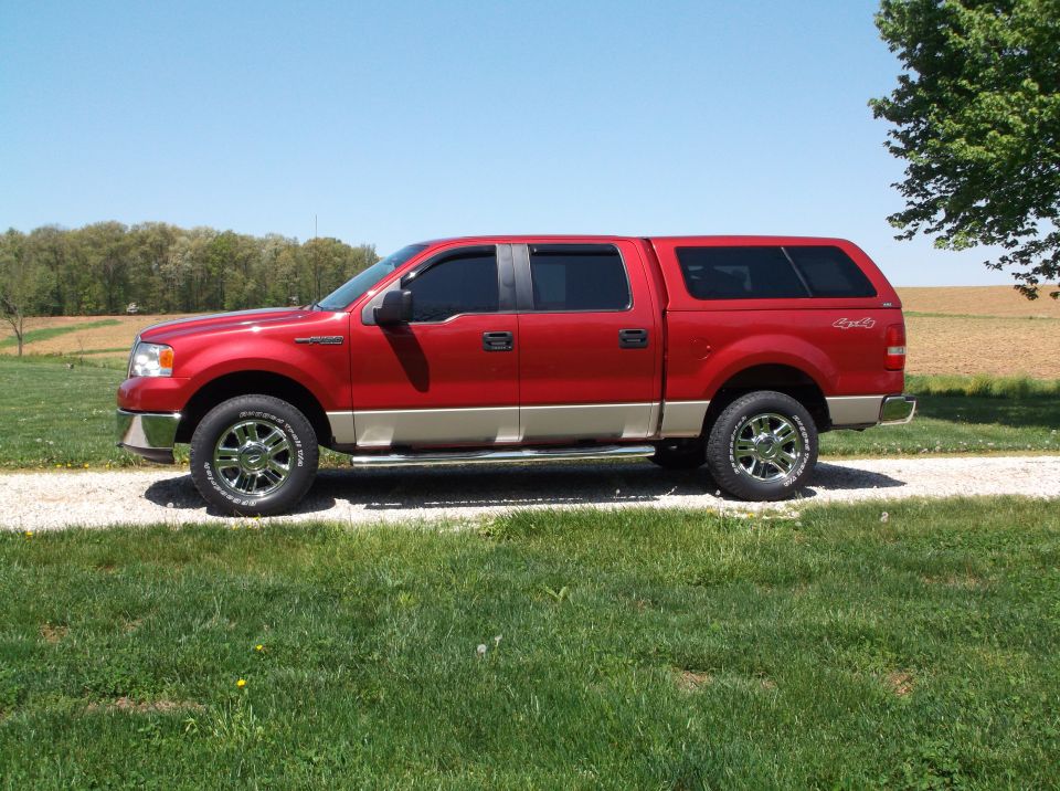 Red pickup truck with a tan lower body and a cap, parked on a gravel driveway
