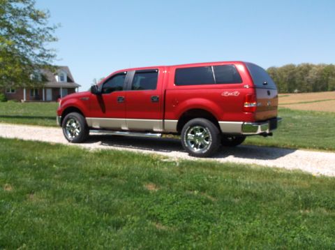 2008 Ford F-150 - A red 2008 Ford F-150 pickup truck with a cap is parked on a gravel driveway next to a grassy field.