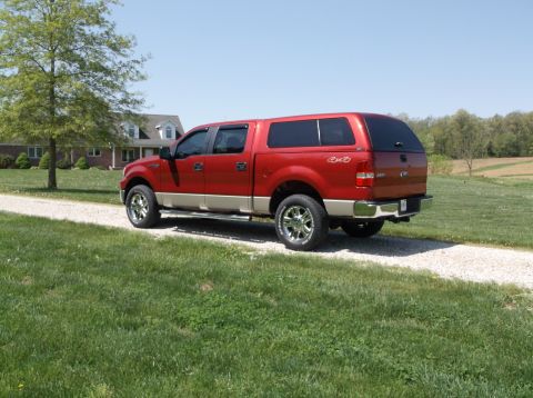 2008 Ford F-150 - Red Ford F-150 pickup truck with a camper shell parked on a gravel driveway in front of a house.