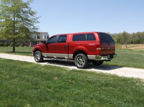 2008 Ford F-150 - A red pickup truck with a tan lower body and a cap is parked on a gravel driveway in front of a house.