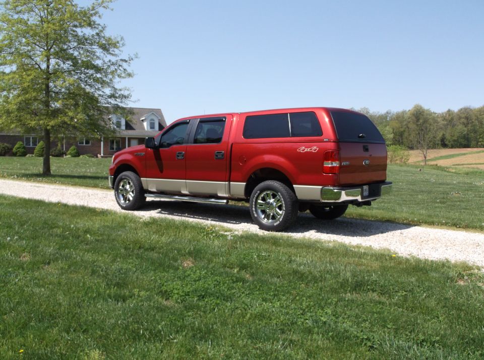 Red pickup truck with a tan lower body and a cap, parked on a gravel driveway
