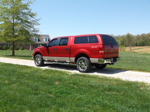 2008 Ford F-150 - Red and tan Ford F-150 truck with a camper shell parked on a gravel driveway.