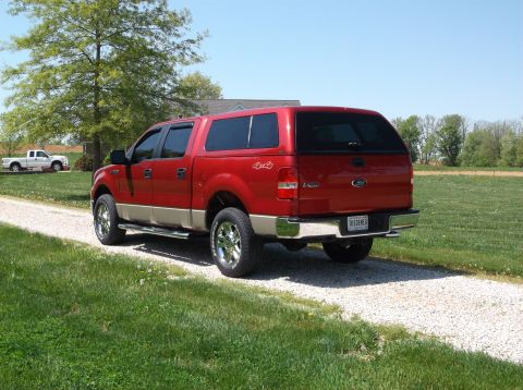 2008 Ford F-150 - This red 2008 Ford F-150 pickup truck is equipped with a tan lower body and a camper shell, seen from the rear.