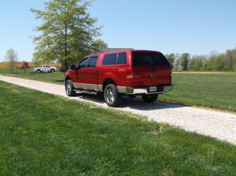 2008 Ford F-150 - Red Ford F-150 pickup truck with camper shell on a gravel driveway, with another truck in the background.