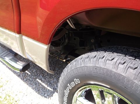 2008 Ford F-150 - Close-up of the rear wheel well of a red and tan pickup truck, showing the tire and suspension components.
