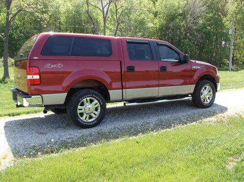 2008 Ford F-150 - This red Ford F-150 pickup truck has a tan lower body and a camper shell, seen from a 3/4 front angle.