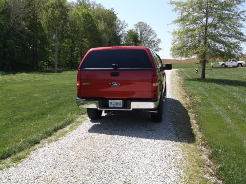 2008 Ford F-150 - Red Ford F-150 pickup truck with a cap on a gravel driveway, with another truck in the background.