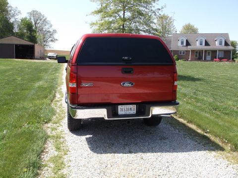 2008 Ford F-150 - Rear view of a red Ford F-150 pickup truck with a camper shell parked on a gravel driveway.
