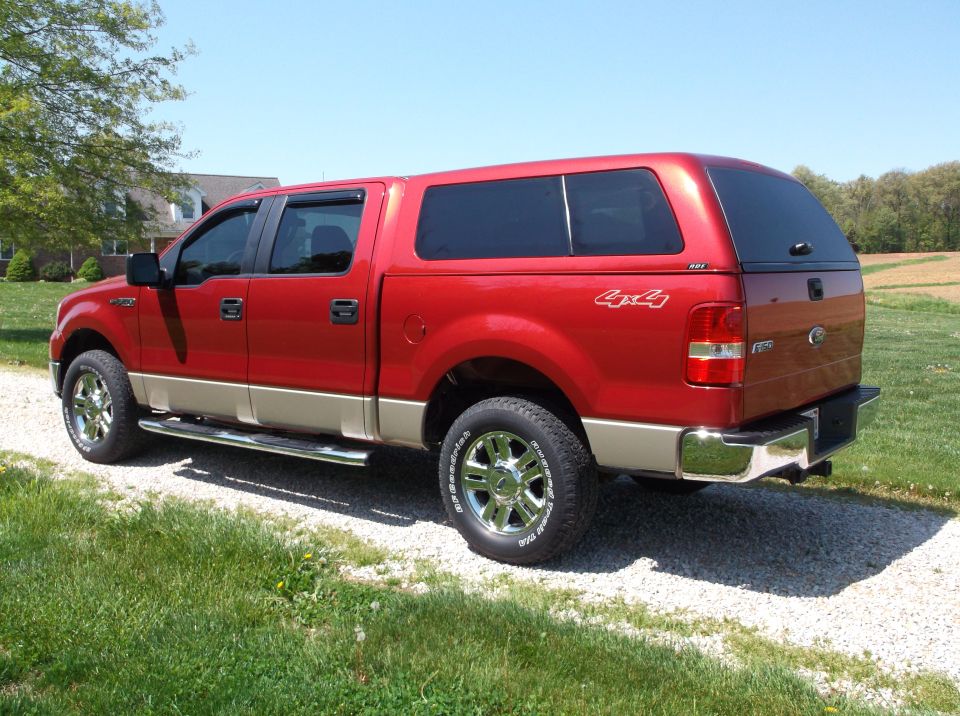 Red Ford F-150 pickup truck with a tan lower body and a camper shell, seen from the rear quarter