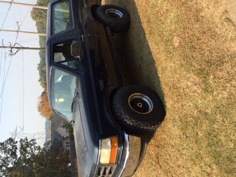 1996 Ford Bronco - This Ford Bronco is parked outdoors on a grassy area with trees and houses in the background.