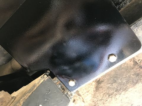 1989 Ford Bronco - This photo shows a close-up of a black painted metal component attached with bolts to the undercarriage of a vehicle.