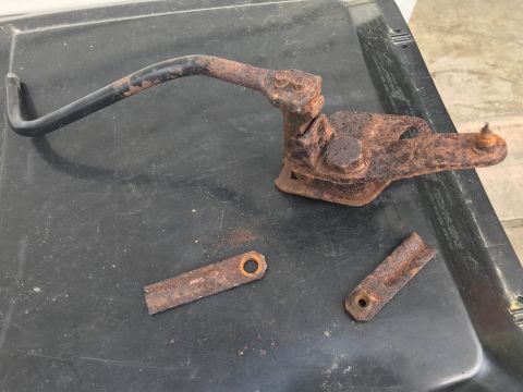 1989 Ford Bronco - Several heavily rusted metal linkage components, likely from a vehicle's transfer case, are laid out on a dark surface.