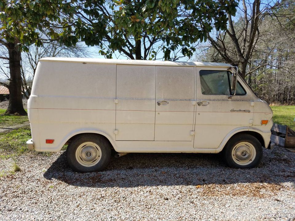 White panel van, side view, dusty exterior, four doors, parked on gravel