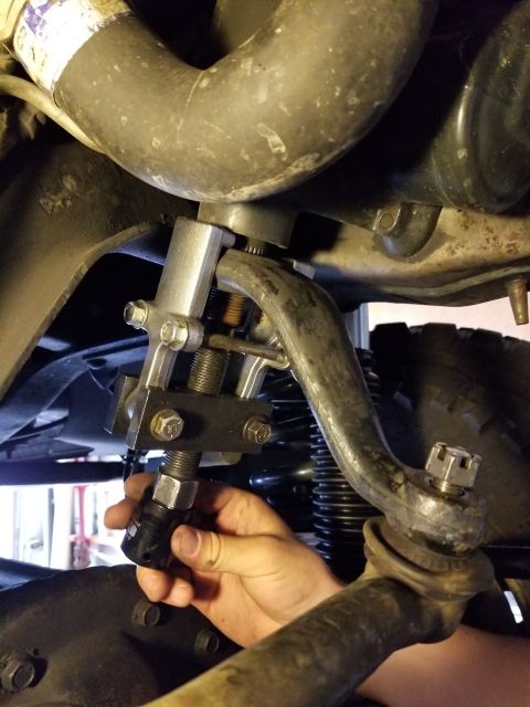 1996 Ford Bronco - A hand uses a tool to adjust the pitman arm on a vehicle's steering linkage, focusing on the mechanical components.