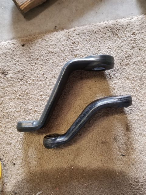 1996 Ford Bronco - Two curved metal steering linkage components are shown resting on a carpeted floor.