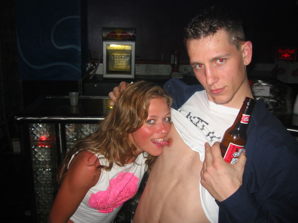 Two people posing at a bar, one holding a beer bottle