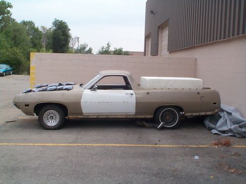 1971 Ford Ranchero - A tan and white 1971 Ford Ranchero is parked outside a building, its hood covered with tarps and a mattress in the bed.