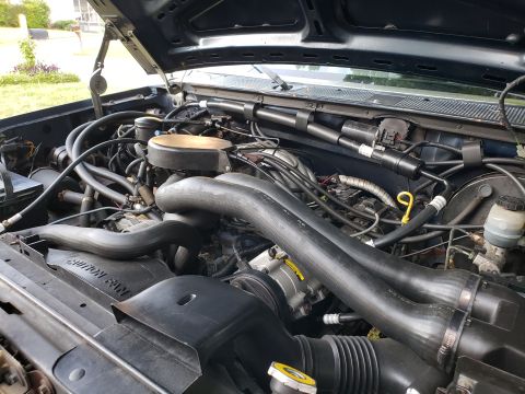1989 Ford Bronco - The engine bay of a 1989 Ford Bronco is visible with the hood open, revealing complex mechanical systems.