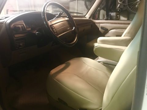 1996 Ford Bronco - The interior of a truck shows tan leather seats and a dashboard with a wood-grain steering wheel.