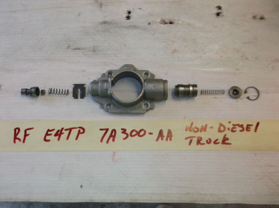 Disassembled brake master cylinder components laid out on a wooden surface. Text on a strip of tape reads 'RF E4TP 7A300-AA NON-DIESEL TRUCK'