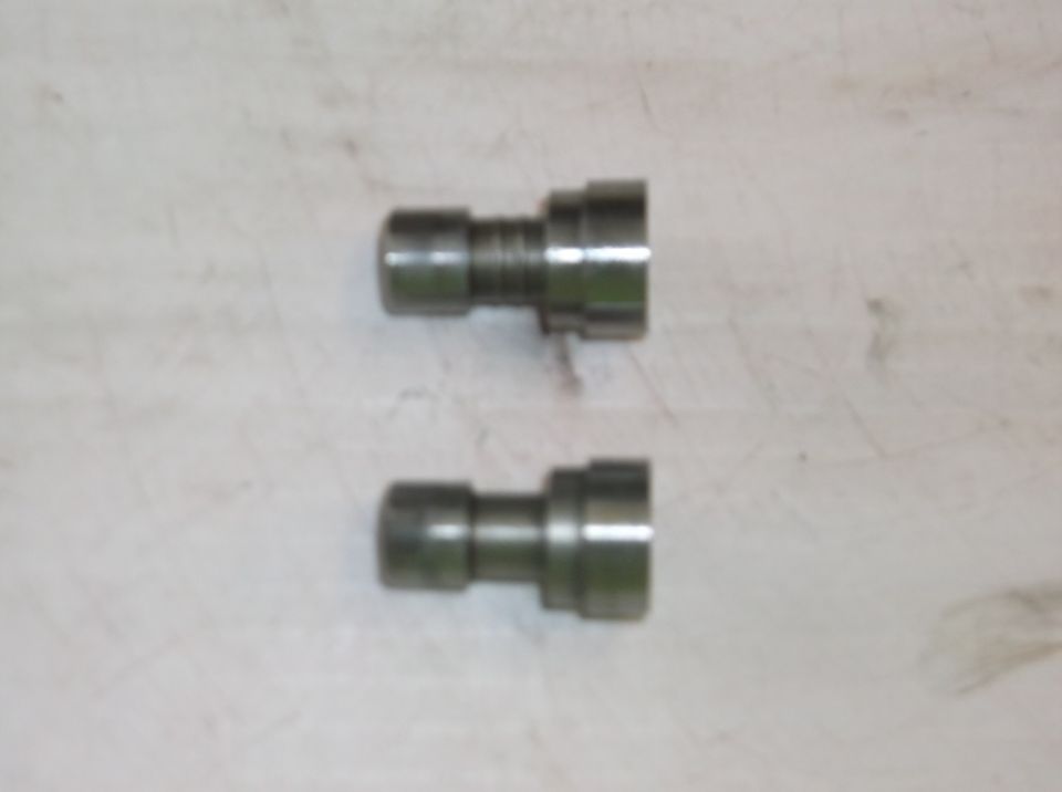 Two metal engine lifters on a light-colored surface