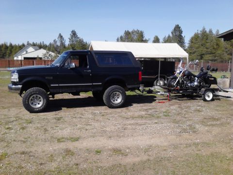 1995 Ford Bronco - A black 1995 Ford Bronco is parked on a gravel lot, towing a trailer carrying a motorcycle.