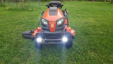 2007 Subaru Impreza - A front view of an orange Husqvarna riding lawn mower with its headlights illuminated on a grassy lawn.